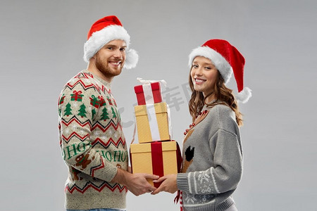 人和假日概念—在丑陋的毛衣聚会圣诞老人帽子的快乐夫妇。快乐的夫妇在圣诞毛衣与礼物