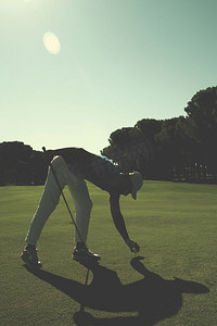 高尔夫球员把球放在球座上。在高尔夫球场风景的美丽的日出在背景中。高尔夫球员将球放置在球座上