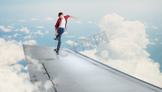 男孩骑滑板上翼。滑板男孩做特技在飞行飞机的边缘