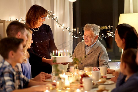 正在燃烧的蜡烛摄影照片_庆祝和家庭概念-快乐的家庭在家中举行生日派对。快乐的一家人在家里开生日派对