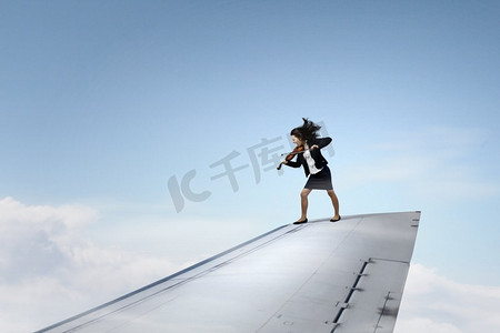 在飞机的机翼上。站在飞机机翼和演奏小提琴的边缘的年轻女商人