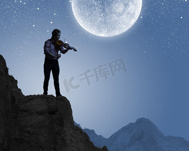 小提琴手。剪影的人演奏小提琴在晚上