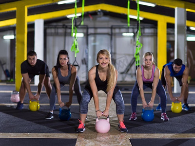 一群健康的年轻运动员在Cross健身工作室用壶铃进行锻炼。运动员拿着壶铃做运动