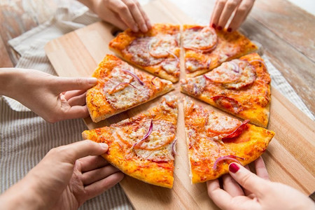 食物、人和饮食理念-在木桌上手拉手分享自制披萨切片。木桌上分享披萨的手的特写