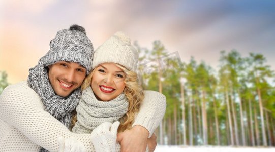 冬天、圣诞节和人们概念快乐的情侣戴着帽子和围巾在森林上空拥抱。一对情侣在冬日森林的背景下拥抱