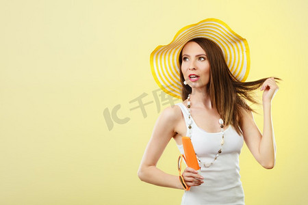 文案背景摄影照片_假日夏日时尚。和护肤理念。戴着黄色帽子的女子手持心形太阳镜防晒霜，背景明亮的文案空间