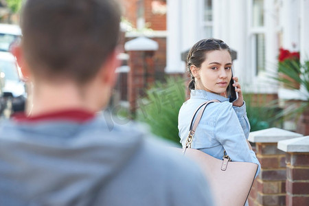 年轻女子在手机上呼叫帮助，同时被男人跟踪在城市街道上