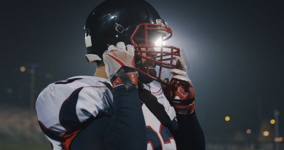 抵御严寒摄影照片_美国橄榄球运动员戴上防护头盔以抵御体育场明亮的照明灯光