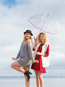 两个时髦的女人穿着时髦的衣服拿着透明的伞花他们的空闲时间户外。两个时尚的女人和伞
