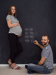 怀孕的夫妇怀孕一周。一对年轻的怀孕夫妇在黑板上用粉笔写下怀孕周