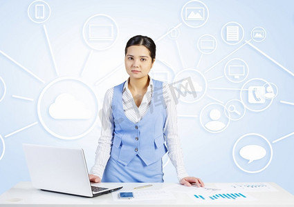 云层上摄影照片_在餐桌旁工作的女人。坐在办公桌前的年轻女商人，背景是笔记本电脑和云计算概念