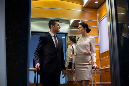商务旅行和人的概念-男人和女人带着旅行包在酒店电梯里。商务团队带着旅行包在酒店电梯里