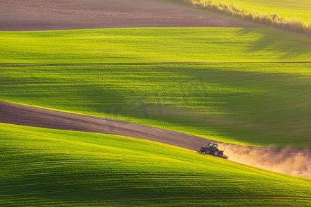 农业景观摄影照片_拖拉机在春天犁地。夕阳光在春天犁拖拉机，南摩拉维亚，捷克共和国
