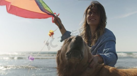 美丽的年轻女子与狗举行风筝在海滩