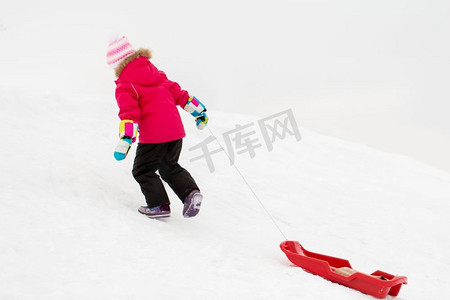 童年，雪橇和季节概念—快乐的小女孩雪橇爬雪山在冬天。小女孩与雪橇在雪山在冬天