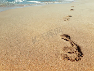 特写在沙滩上靠近水的脚印。旅程概念