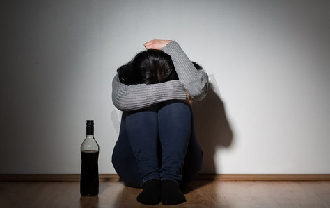 抑郁症妇女摄影照片_酒精中毒，抑郁症和人概念-有瓶酒的不愉快的妇女哭在家里。一个拿着酒瓶在家里哭的女人