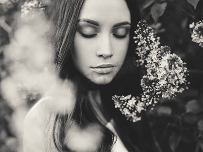 被丁香花朵包围的美丽年轻女子的黑白户外时尚照片。春暖花开