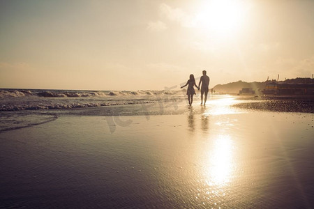 洛阳剪影摄影照片_沿着沙滩漫步，欣赏日落的恩爱夫妇的剪影。海岸线上的年轻浪漫情侣