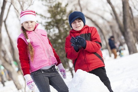 可爱的男孩和女孩在冬季公园堆雪人。冬季活动小游戏