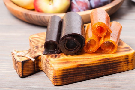 秋天木板背景摄影照片_在木板、李子和苹果上烘干水果皮革。干果皮革