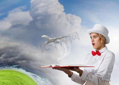 这本书能激发你的想象力。年轻女子在白色帽子与打开的书在手中和飞机飞出去