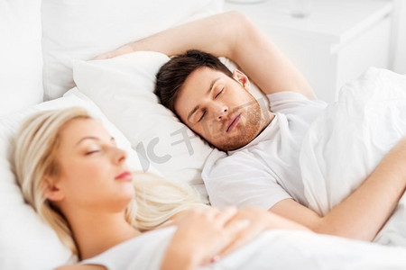 宝宝床上摄影照片_人，休息和关系概念—幸福的夫妇睡在家里的床上。幸福的夫妇睡在床上在家里