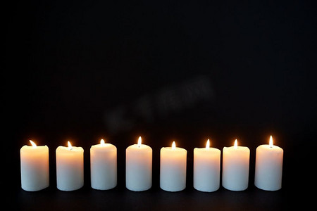 纪念抗日战争胜利75周年摄影照片_哀悼和纪念的概念-蜡烛在黑暗中燃烧在黑色的背景上。黑暗中燃烧的蜡烛覆盖着黑色的背景