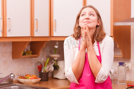 愿景和理念。快乐的梦想思考的女人在厨房。穿着粉红色围裙的家庭主妇在家里。梦想家庭主妇在家里