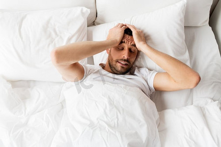 人，就寝时间和休息的概念—男人躺在床上，在家里患有头痛或宿醉。一名男子在家中因头痛而卧床