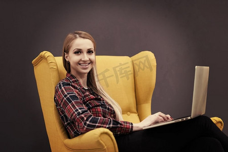黄色企业摄影照片_初创企业，在现代办公室用笔记本电脑工作的女人，坐在有创意的黄色扶手椅上