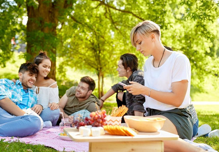 休闲、科技和人的概念-女性在夏令营与朋友野餐时使用智能手机。与朋友野餐时使用智能手机的女性