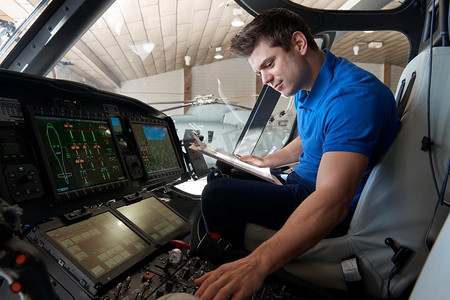 带剪贴板的男性航空工程师在直升机驾驶舱内工作