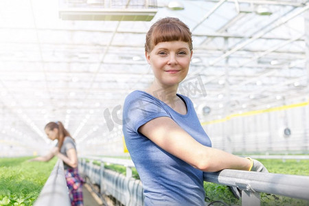肖像微笑的女性植物学家站在过道在植物苗圃