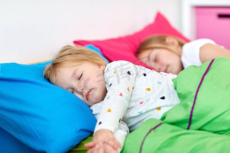 童年，睡觉时间和家庭概念-快乐的小女孩或姐妹睡在家里的床上。快乐的小女孩们睡在家里的床上