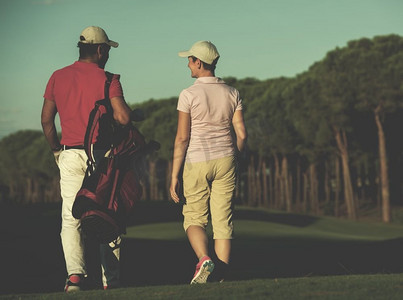 一对年轻夫妇在高尔夫球场上走向下一个球洞。一个拿着高尔夫球包的男人。走在高尔夫球场上的情侣