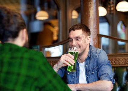 人，休闲和圣帕特里克节的概念-快乐的男性朋友在酒吧或酒吧喝绿啤酒。在酒吧或酒吧喝绿啤酒的男性朋友