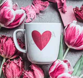 爱情观摄影照片_桌子背景上有心形和粉色郁金香的白色马克杯，顶视。春节问候与爱情观