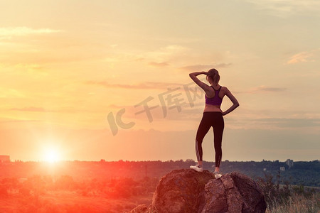年轻的运动妇女与手臂提出在日落在夏天