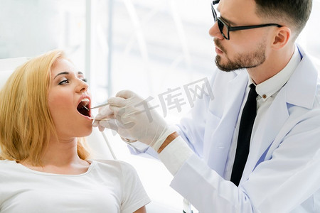 年轻英俊的牙医检查愉快的妇女病人的牙齿坐在牙医椅子在牙科诊所。牙科护理概念。