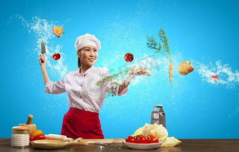 亚裔女厨师用刀做饭。亚洲女厨师在空中用刀切水果和蔬菜