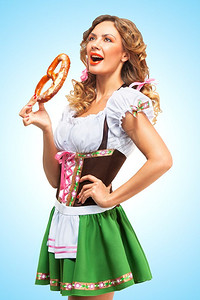 年轻性感的啤酒节女子穿着传统的巴伐利亚连衣裙，在蓝色背景下吃着椒盐卷饼。
