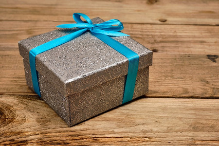 丝带盒摄影照片_礼物生日圣诞礼物概念-银色礼品盒，旧木质背景上有蓝丝带。蓝丝带礼品盒