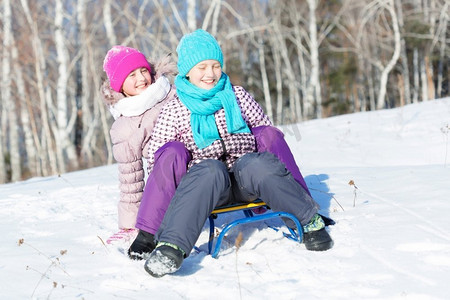 冬天的乐趣。两个可爱的女孩享受雪橇乘坐在美丽的多雪的冬季公园