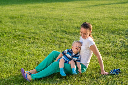 快乐的女人和孩子在草地上玩得很开心。公园里母子俩在绿茵茵的草地上休息的家庭生活场景。
