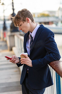 男性年轻成年青少年穿着西装和领带使用智能手机为社交媒体和喝外卖咖啡