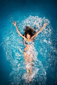 一位性感的皮肤黝黑的女士，穿着五颜六色的比基尼躺在游泳池里。