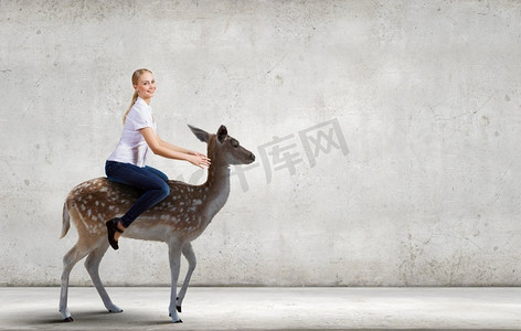 年轻漂亮无畏的女人骑着鹿的动物。女骑鹿