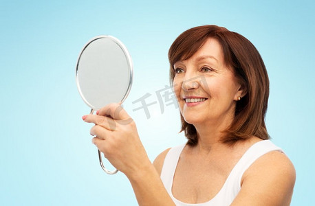 老年镜摄影照片_美丽和老人概念—微笑的高级妇女象象有镜子在蓝色背景肖像微笑的高级妇女与镜子