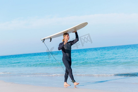 波澜摄影照片_一名年轻的冲浪者在海滩上挥舞着冲浪板。准备好掀起波澜